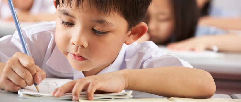 “student-writing-at-desk-in-classroom“