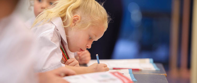 “student-writing-at-desk-in-classroom“