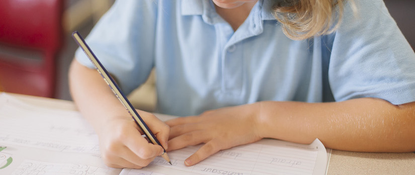 “student-writing-at-desk-in-classroom“