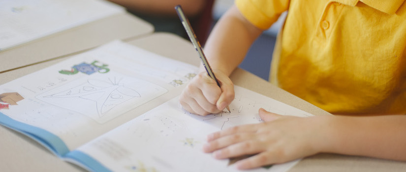 “student-using-writing-time-book-at-desk-in-classroom“